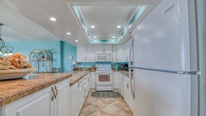 A kitchen with white cabinets, a granite countertop, a white refrigerator, and a microwave. - Surfmaster 103 - Three-bedroom, three-bath first-floor oceanfront condo (Garden City Beach)