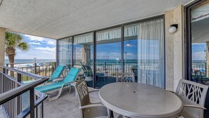 A balcony with a table and chairs, overlooking a beach with umbrellas and lounge chairs. - Surfmaster 103 - Three-bedroom, three-bath first-floor oceanfront condo (Garden City Beach)