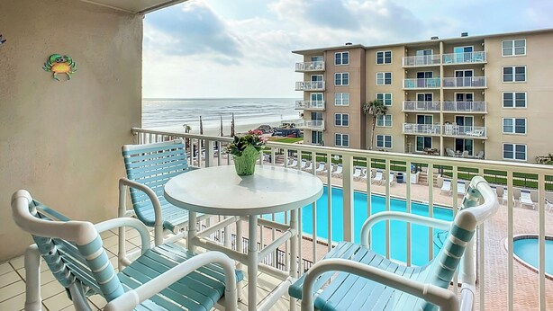 Ein Balkon mit Pool, Stühlen und Blick auf das Meer und ein Gebäude.
