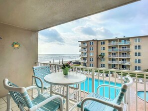 A balcony with a pool, chairs, and a view of the ocean and a building.