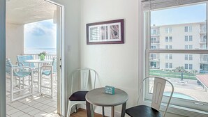 Ein Balkon mit Blick auf den Ozean und ein Gebäude. Zwei Stühle und ein kleiner Tisch mit einem Schild sind vorhanden.