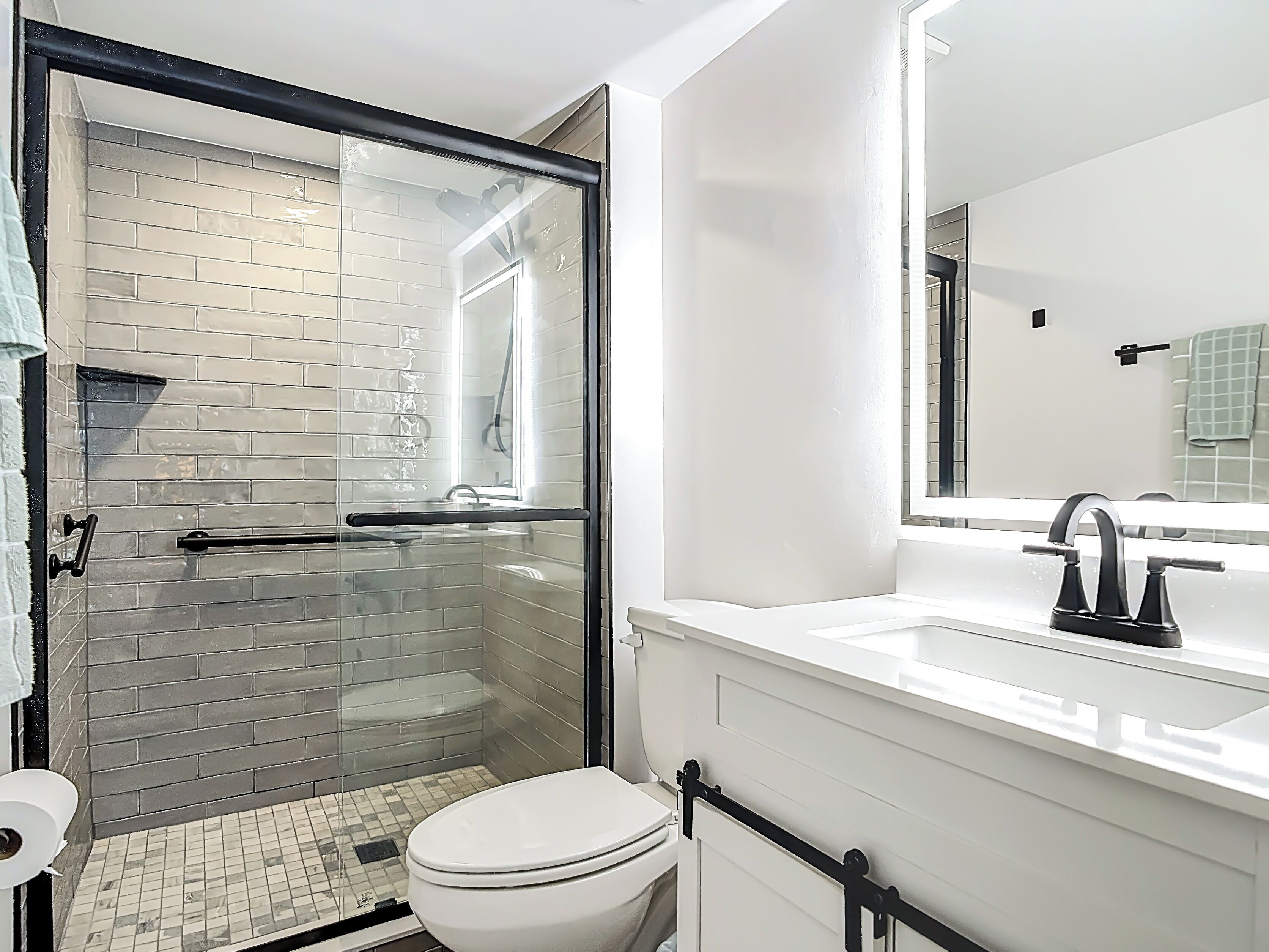 Ein Badezimmer mit Duschkabine aus Glas, Toilette in Weiß und Waschbecken mit Spiegel.