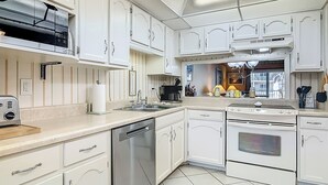A modern kitchen with white cabinetry, a dishwasher, an oven, and a toaster. - 2bed/2ba Ocean view condo on No drive Beach in NSB! (New Smyrna Beach)