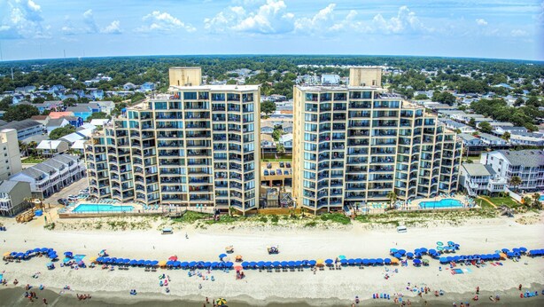 A beachfront hotel with multiple high-rise buildings, a sandy beach, and a pool area. - Surfmaster 1108 - Three-bedroom, three-bath oceanfront condo (Garden City Beach)