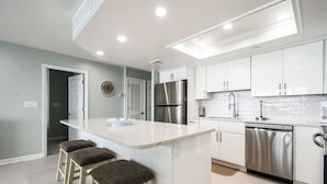 A modern kitchen with white cabinets, stainless steel appliances, and a central island with stools. - Surfmaster 1108 - Three-bedroom, three-bath oceanfront condo (Garden City Beach)