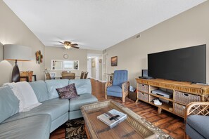 A living room with a sofa, armchairs, a coffee table, a television, and a ceiling fan. - Watch the sunrise over the No Drive Beach in NSB! (New Smyrna Beach)