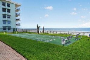 A green shuffleboard court with a warning sign, a bench, and a view of the ocean. - Watch the sunrise over the No Drive Beach in NSB! (New Smyrna Beach)