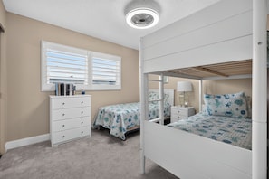 A bedroom with bunk beds, a dresser, a window with blinds, and a ceiling fan. - Watch the sunrise over the No Drive Beach in NSB! (New Smyrna Beach)