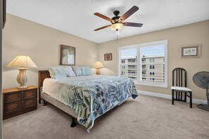 A bedroom with a bed, two bedside lamps, a ceiling fan, a window with blinds, and a chair.