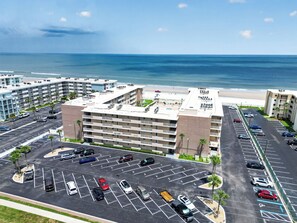 A multi-story hotel with a parking lot, beachfront view, and a pool area.