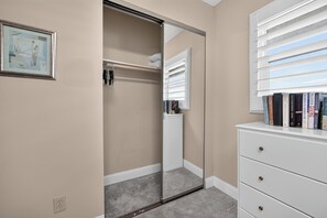 A room with a walk-in closet, a white dresser with books, and a framed picture on the wall.