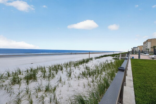 A beach with a grassy area, a walkway, and a building in the background.