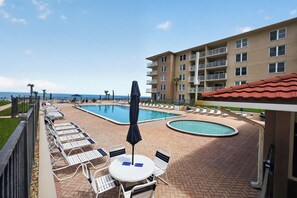 A pool area with lounge chairs and umbrellas, a separate circular pool, and a view of the ocean.