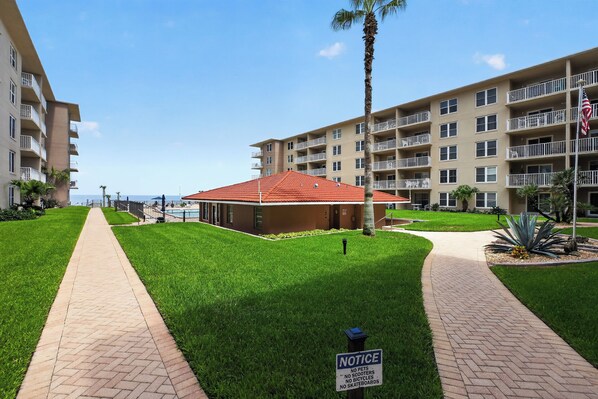 A residential building with a red-roofed structure in the center, surrounded by well-maintained lawns and a clear sky.