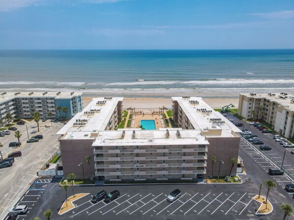 A multi-story hotel with a rooftop pool, parking lot, and ocean view. - Watch the sunrise over the No Drive Beach in NSB! (New Smyrna Beach)