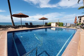 A swimming pool with lounge chairs and umbrellas, a view of the ocean, and a stone wall.