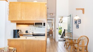 Une cuisine compacte avec des meubles en bois, un four à micro-ondes et une machine à café. On y trouve également un coin repas avec une table en verre et des chaises en osier.