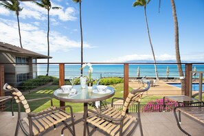 A terrace with a table set for two, overlooking a pool and the ocean.