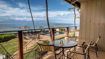 A balcony with a view of the ocean, outdoor seating, and a pool area.