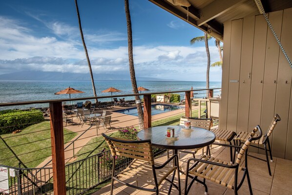 A balcony with a view of the ocean, outdoor seating, and a pool area.