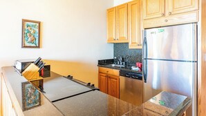 A compact kitchen with wooden cabinets, a stainless steel refrigerator, and a granite countertop. - Top Floor! Direct Ocean View! Vaulted Ceilings! Winter Spec! #218 (Lahaina)