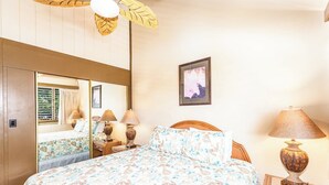 A bedroom with a bed, bedside tables, lamps, a mirror, and a framed picture on the wall. - Top Floor! Direct Ocean View! Vaulted Ceilings! Winter Spec! #218 (Lahaina)