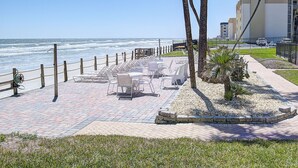 Eine Strandterrasse mit Sitzgelegenheiten im Freien, Palmen und Blick aufs Meer.