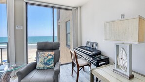Una habitación con vista a la playa, un piano, una silla, un sofá y una mesa de vidrio.