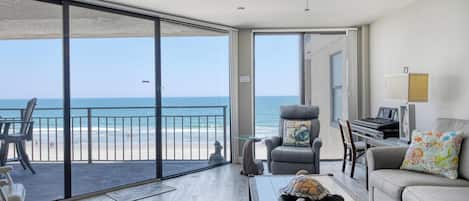 Une chambre avec vue sur la plage, un ventilateur de plafond, un piano et une tortue posée sur une table basse.