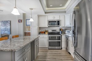 A modern kitchen with stainless steel appliances, white cabinetry, and a granite countertop.