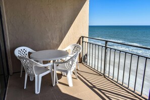 A balcony with a table and chairs, overlooking the sea.