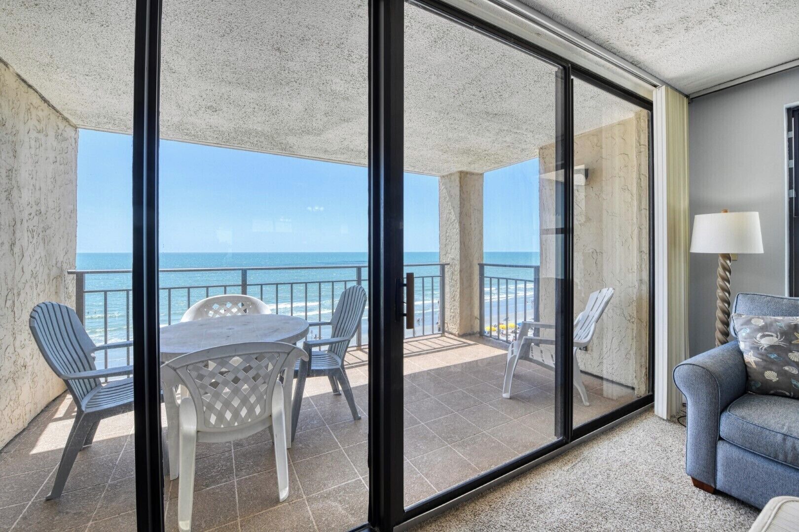 A balcony with a view of the ocean, a dining table with chairs, and a sofa.
