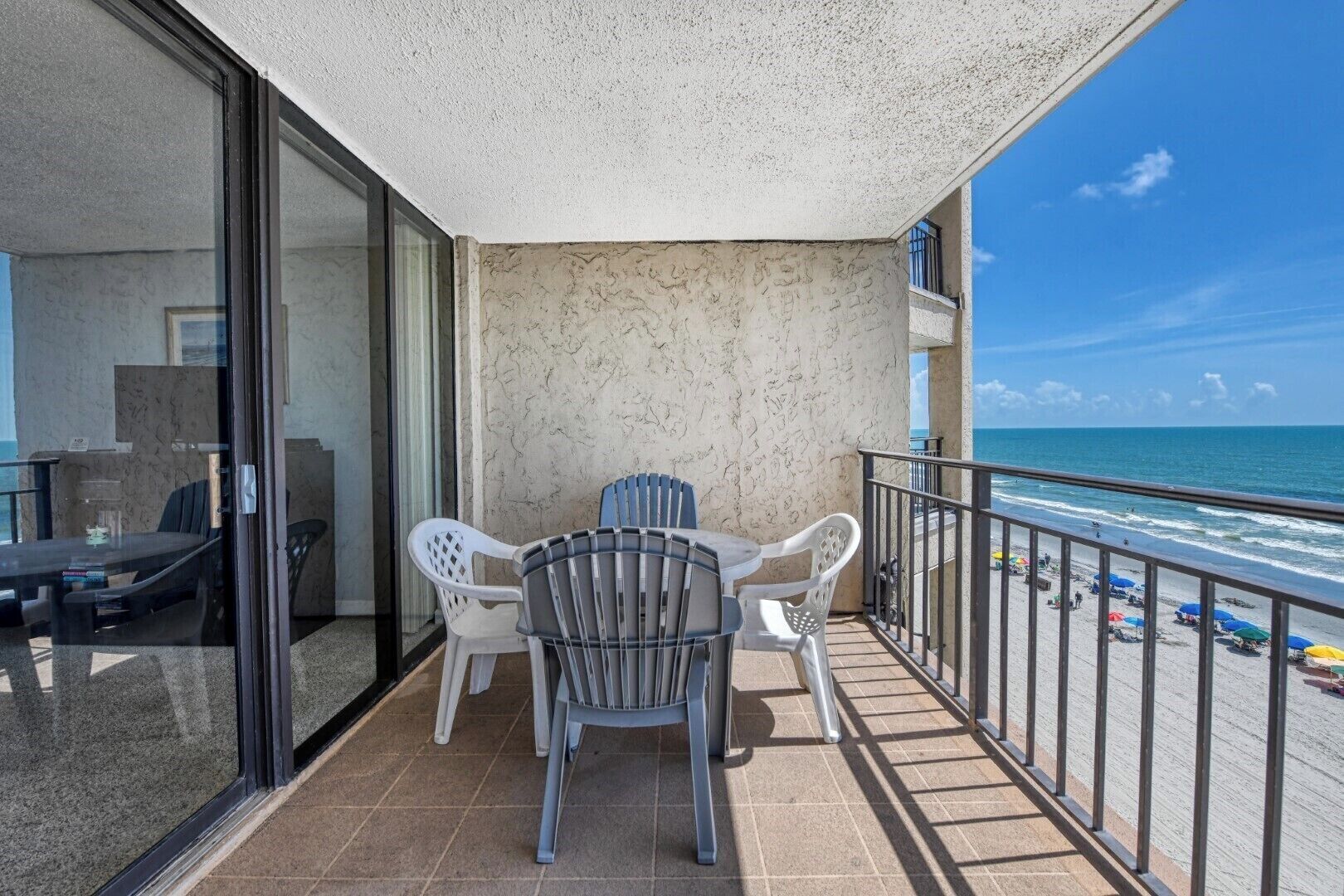 Un balcon avec une table et des chaises, une porte vitrée et une vue sur la plage.