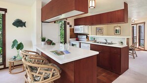 A modern kitchen with a central island, wooden cabinets, and a large window. - Waikomo #320 - 2 Bed in Poipu Lush Landscaping Walking distance to Beach & Pool (Koloa)