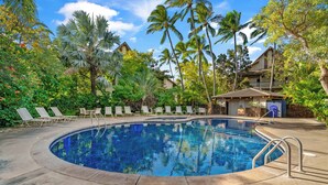 A circular pool with lounge chairs, palm trees, and a building with a balcony. - Waikomo #320 - 2 Bed in Poipu Lush Landscaping Walking distance to Beach & Pool (Koloa)