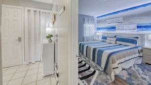 A bedroom with a bed, a nightstand, a wall-mounted TV, and a window with curtains. - Surfmaster 606 - One Bedroom, One 1/2 Bath Oceanfront Condo (Garden City)