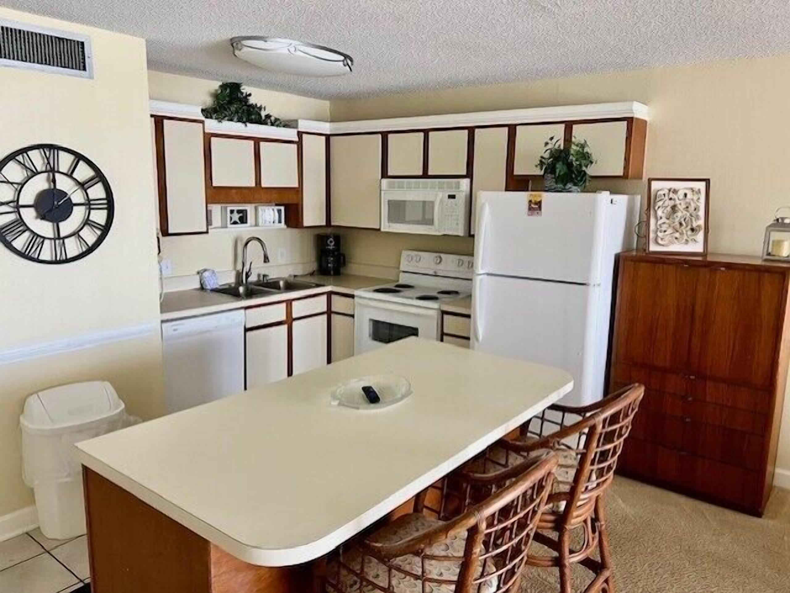A compact kitchen with a central island, a microwave, a stove, and a refrigerator. There are two bar stools at the island.