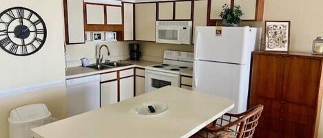 A compact kitchen with a central island, a microwave, a stove, and a refrigerator. There are two bar stools at the island.