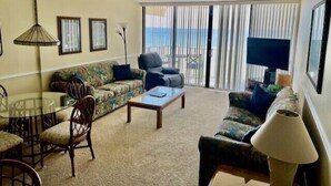 Un salón con sofá, una mesa de centro, televisor y un balcón con vistas.