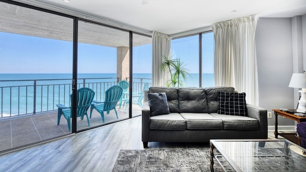 Un salon moderne avec un canapé gris, des fauteuils turquoise et une table basse en verre.
