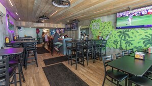 A restaurant with wooden ceiling beams, a large screen displaying a golf event, and a green wall with a 'Salty Pickle' sign. - Cozy 2 Bedroom Oceanfront Condo (MURRELLS INLET)