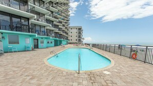 A pool area with a tiled deck, a pool, and a view of the ocean. - Cozy 2 Bedroom Oceanfront Condo (MURRELLS INLET)
