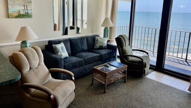 A living room with a sofa, two armchairs, a coffee table, and a large window with a view of the ocean. - Cozy 2 Bedroom Oceanfront Condo (MURRELLS INLET)