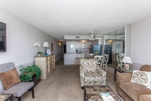 A living room with a sofa, a coffee table, and a dining area with chairs. There is a kitchen in the background with a refrigerator and a microwave. - COZY 1 BEDROOM CONDO IN GARDEN CITY (MURRELLS inlet)