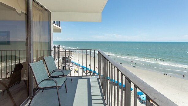 A balcony with a view of a beach, equipped with chairs and umbrellas. - COZY 1 BEDROOM CONDO IN GARDEN CITY (MURRELLS inlet)
