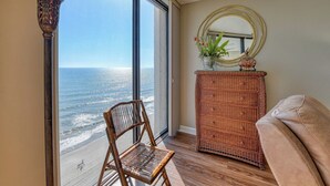 A room with a large window overlooking the ocean, a wicker dresser, a chair, and a round mirror on the wall. - Surfmaster 904 - Two-bedroom, two-bath oceanfront condo with pools (Garden City Beach)