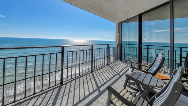A balcony with a view of the ocean, metal railing, and two wooden chairs. - Surfmaster 904 - Two-bedroom, two-bath oceanfront condo with pools (Garden City Beach)