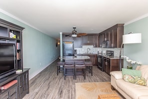 A modern kitchen with dark wood cabinets, a central island, and a dining area with leather chairs.