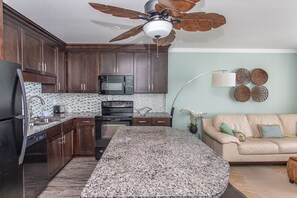 A modern kitchen with dark wood cabinets, a granite countertop, a built-in microwave, and a ceiling fan.