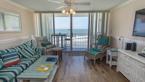 A living room with a sofa, armchair, and a small table. There is a ceiling fan and a TV mounted on the wall. - Beautiful Ocean Front 3 Bedroom Condo (Murrells Inlet)